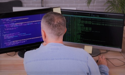 Rückansicht eines Mannes vor zwei Computerbildschirmen